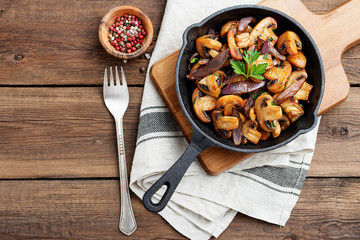 Fried mushrooms with fresh herbs in black cast iron pan.