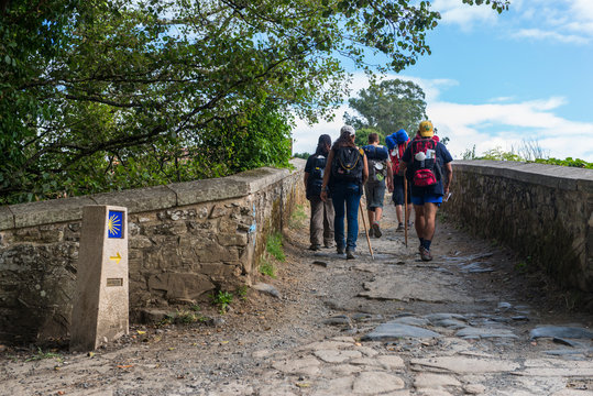 FURELOS, SPAIN - JULY 31, 2016: Some young pilgrims with backpacks cross a medieval bridge, making the Camino de Santiago.