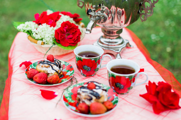 Samovar with a cup of morning tea, cinnamon buns and strawberry on the table on nature background