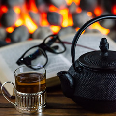 Obraz na płótnie Canvas Cup of tea and open book in front of warm fireplace. 