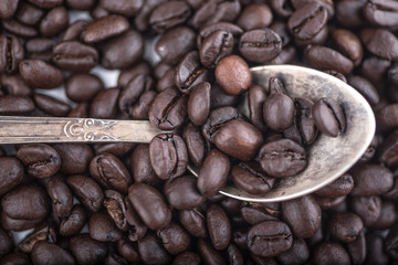 Roasted coffee beans in Old silver vintage dessert  spoon on brown  coffee beans background. Top view, Close up.