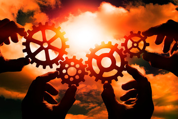 gears in the hands of people on the background of the evening sky. mechanism, interaction, teamwork.
