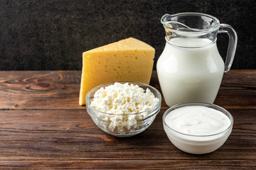 Dairy products on dark wooden background. Milk, kefir, cheese, cottage cheese, butter and sour cream.