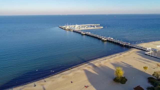 Sopot resort in Poland with wooden pier, marina, yachts and sandy beach. Aerial 4K approaching video in sunset light.