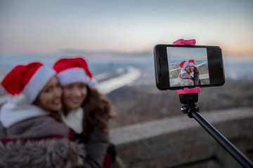 Two beautiful young women taking a selfie outside with a city in the background