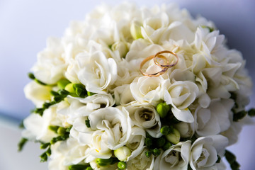 A pair of wedding rings on a bouquet of white flowers, close up shot