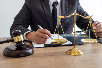Legal law, advice and justice concept, counselor lawyer or notary working on a documents and report of the important case and wooden gavel, brass scale on table in courtroom