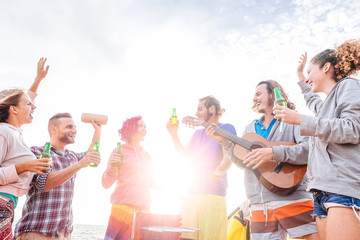 Happy friends drinking beers and playing guitar at barbecue on the beach - Group of young people having fun and laughing together at bbq party - Travel, vacation and youth holidays lifestyle concept