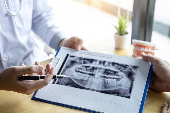 Image of doctor or dentist presenting with tooth x-ray film recommend patient in the treatment of dental and dentistry, working at workplace