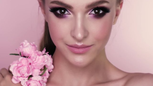 beauty portrait of a beautiful girl with makeup and flowers. closeup shot in studio on a pink background