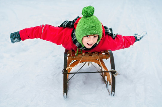 Happy child riding down a hill on an old wooden sled. Winter out