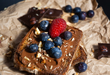  Delicious chocolate bread toast with chocolate spread and bluberry and nuts toppings on rustic paper with black background