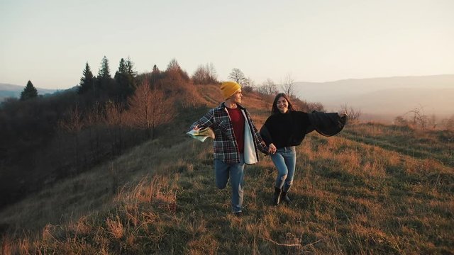 Couple in love hiking outdoors. Hikers man and woman trekking running with backpacks in trail with map at sunset in mountains