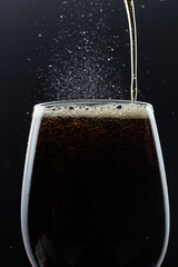 Glass of pouring fizzy drink with ice on a black background