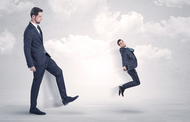 Big businessmen kicking himself as a small employee with cloudy background
