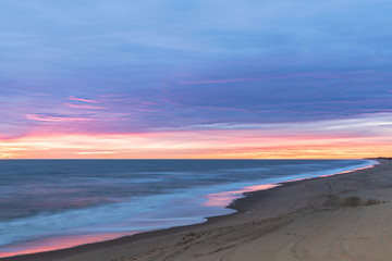 Fototapeta na wymiar Sunrise along the Atlantic Ocean in Virginia Beach at Little Island Park in Sandbridge. The sun creates pink and purple pastel reflections on the surf