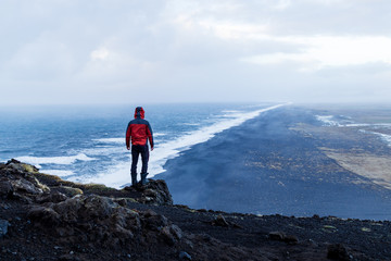 Person standing at Dyrholaey lighthouse in Iceland looking out over the black sand beach below...