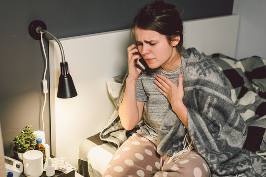 respiratory diseases and home remedies. young woman sick with cold sitting bedroom on bed holding throat sadness emotion. Sore throat man takes pills. Call phone, ask for help doctor. Call ambulance