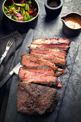 Traditional smoked barbecue wagyu beef brisket offered as top view on an old cutting board with...