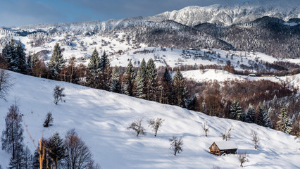Mountain lodge in the picturesque Romania`s country side on a cold winter morning. Pristine clear ski  and snowy mountain peaks in the background.