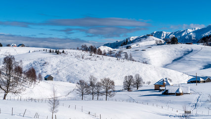 Fototapeta na wymiar Mountain lodge in the picturesque Romania`s country side on a cold winter morning. Pristine clear ski and snowy mountain peaks in the background. Piatra Craiului National Park.