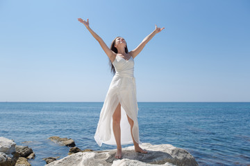 Girl in wedding dress posing against sea with arms outstretched