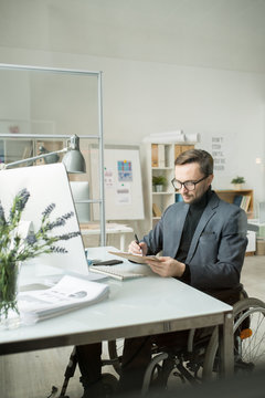 Serious Disabled Businessman In Eyeglasses Doing Paperwork At His Workplace In Front Of Computer At Modern Office