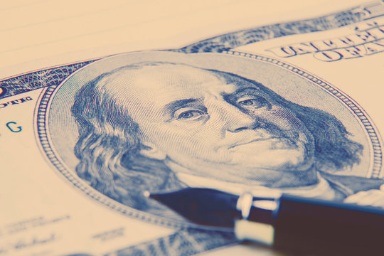 Stock market prices concept. Hundred US Dollar bill and a pen on a notebook background. Macro image.