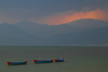 Sunset during rain in Pokhara, Nepal. Boats in the lake with mountains visible in the background through the mist.