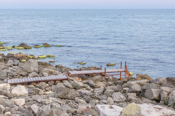 Wooden bridge to the sea. Ocean coast. Place of solitude. The path to the sea. The edge of the world. Stone beach. Fishing pier. Pier for boats. The coastline of the Black Sea.