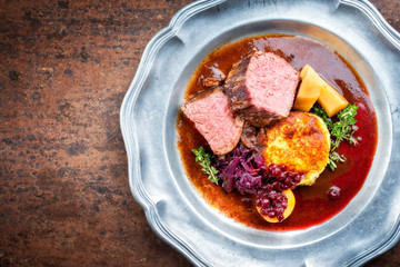 Traditioneller gebratener Hirschrücken mit Kartoffel Püree und Rotkohl Kraut in Rotwein Wild Sauce als Draufsicht in einem Zinnteller  mit Textfreiraum links