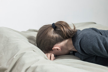 A depressed woman cries with her hands covering her face, lying on the couch.