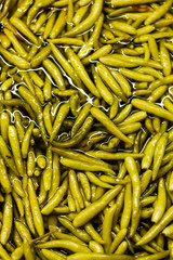 Marinated green peppers in water on the counter in the supermarket. Glare around the peppers.