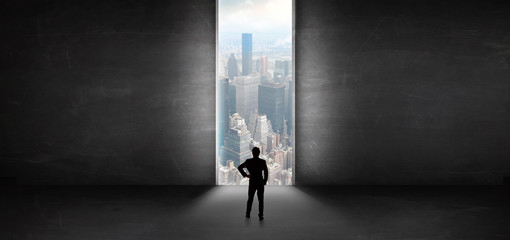 Businessman standing in a dark room and looking outside to a cityscape view
