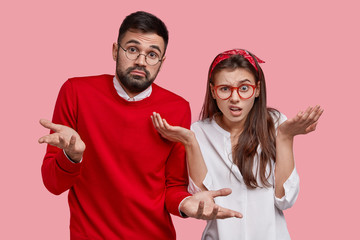 Two hesitant unshaven man and dissatisfied woman shrug shoulders, feel unsure, have doubt while...