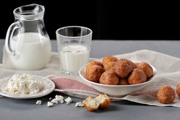Fried in cottage cheese balls in a deep plate. Next to him is a plate with a taorus, a glass and a jug with milk. Close-up. Dark background.