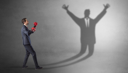Fototapeta premium Businessman with boxing gloves fighting with disarmed businessman shadow 