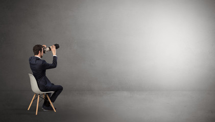 Businessman staying in an empty grey dark room with stuffs on his lap
