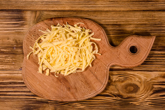 Cutting board with grated cheese on wooden table. Top view