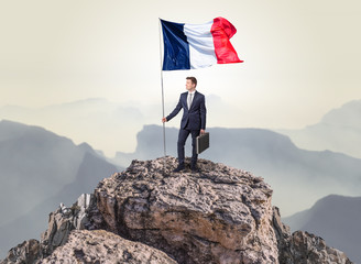 Successful businessman on the top of a mountain holding France victory flag
