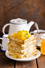 Homemade thin crepes with orange jam, stack of pancakes on wooden rustic background