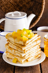 Homemade thin crepes with orange jam, stack of pancakes on wooden rustic background