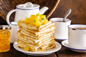 Homemade thin crepes with orange jam, stack of pancakes on wooden rustic background