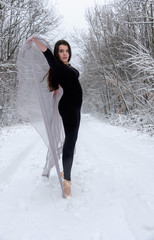 Junge schöne Frau Mädchen in schwarzem Ballett Anzug im verschneiten Winter Wald reckt sich und steht auf Zehen Spitze in Ballettschuhen