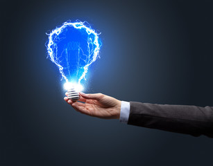 Hand holding shiny light bulb on dark background. New idea concept