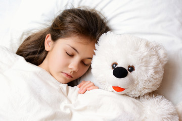 Beautiful charming small child with messy long hair lies sleeping with teddy bear on comfortable bed