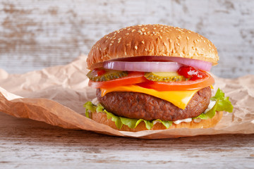 Hamburger in wrapping paper on wood background.