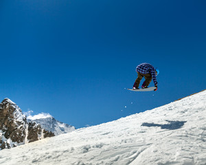 Jumping snowboarder keeps one hand on the snowboard on blue sky background