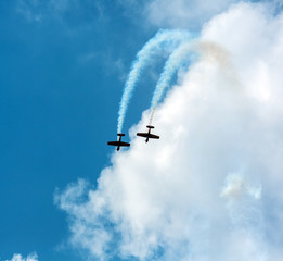 Fototapeta na wymiar Silhouette sport aircraft with propellers, performing tricks with a smokescreen against the blue sky in the air show performance