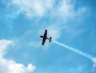 Silhouette sport aircraft with propellers, performing tricks with a smokescreen against the blue...